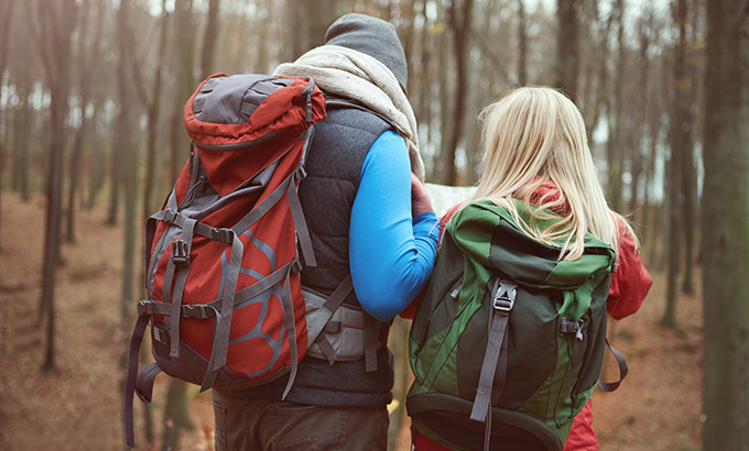 couple hiking in forest looking at map with backpacks exploring nature together