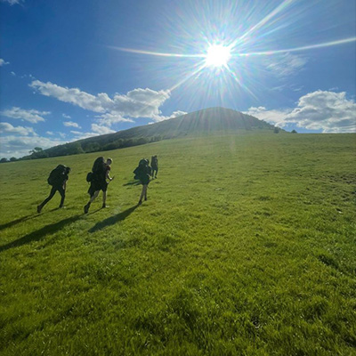 hikers climbing a grassy hill under a bright sun surrounded by clouds experiencing adventure in nature 17 miles trail