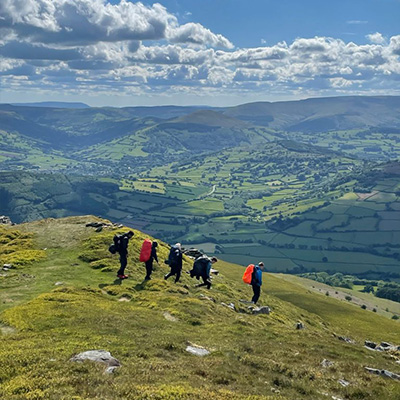 group of hikers climbing a mountain with green valleys and blue sky in the background exploring scenic landscapes and enjoying outdoor adventure 3 hiking trails