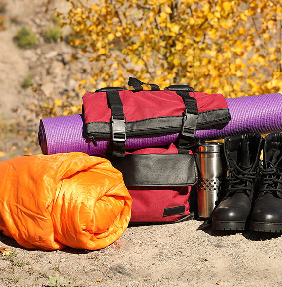 camping gear including an orange sleeping bag a red backpack purple yoga mat a silver water bottle and black hiking boots perfect for adventure 7 essentials for outdoor trips