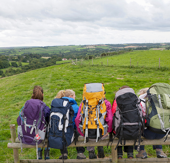 group of hikers with backpacks sitting on a fence overlooking lush green hills and a cloudy sky enjoying nature and adventure on a seven day trip